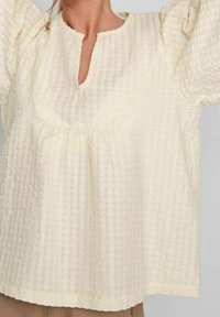 Ljuscremefärgad blus i texturerat tyg med rutmönster. Har rund halsringning och puffärmar, något lös passform.