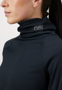 Sort, langærmet atletisk top med høj krave, der har tekstureret stof og et lille gråt logo på halsen, hvilket fremhæver det tætsiddende design.