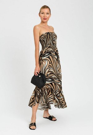 Donna in piedi con abito senza spalline con stampa animalier, che tiene una pochette nera testurizzata, indossa sandali neri a ciabatta con fibbia dorata.