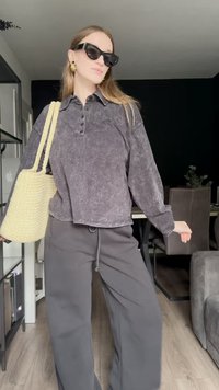 Svetlo siva teksturirana dolga majica z dolgimi rokavi in detajli na gumbih, v kombinaciji s temno sivo širokosrajno hlačami. Izgled dopolnjuje svetlo rumena groba pletena torba in sončna očala v obliki mačjih oči.