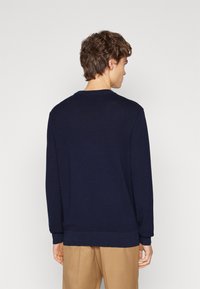 Maglione lavorato a maglia blu navy con maniche lunghe e scollatura a girocollo. Presenta polsini e orlo a coste. Tessuto leggero con una vestibilità classica.