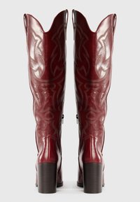 Punaiset nahkakengät cowboy-tyyliin, joissa on terävä kärki, koristeompeleita ja paksu korko. Sivussa vetoketju.