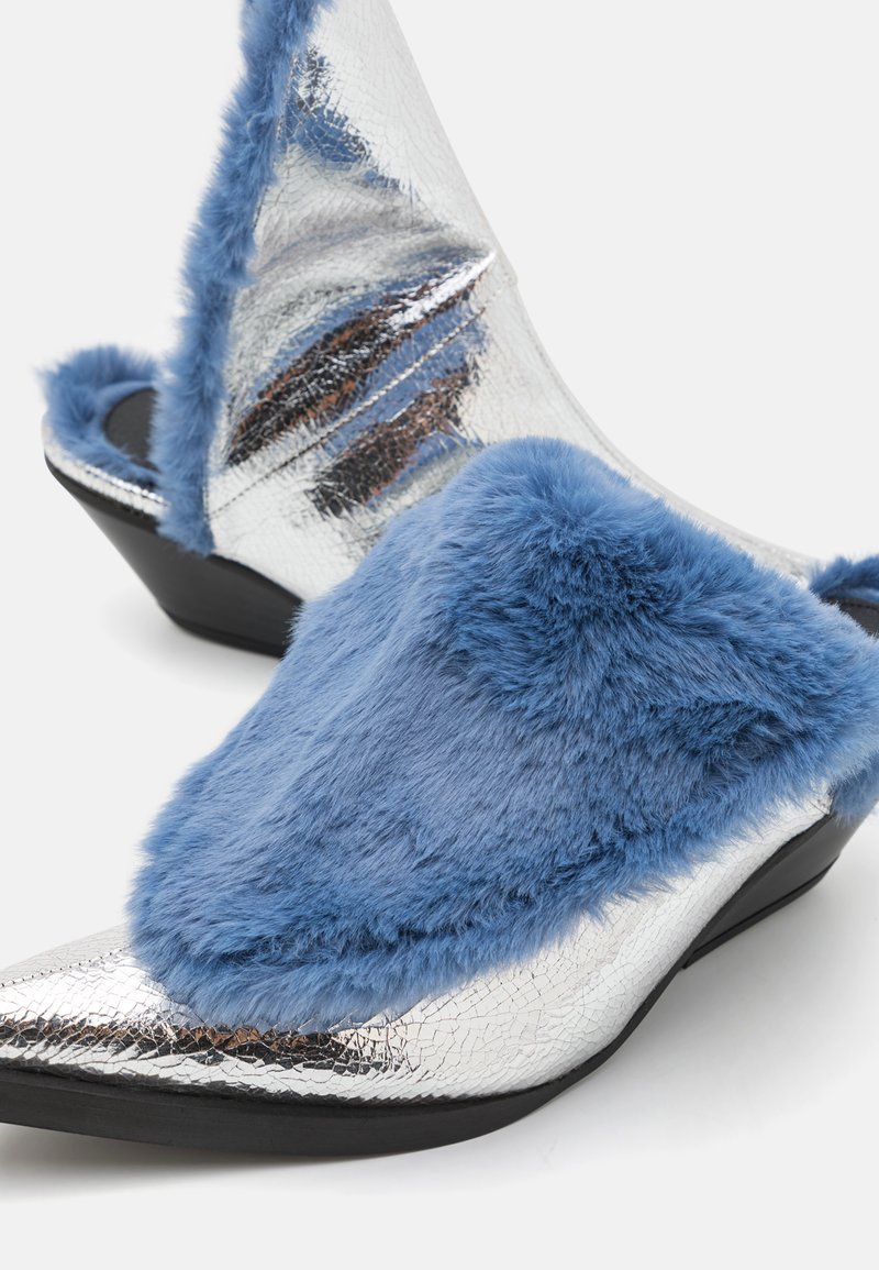 Silverfärgade metallictofflor med spetsig tå, prydda med mjuka blåa faux fur-overlay och en kilklack med en sprucken yta.