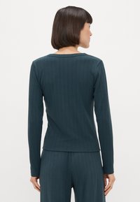 Ciepła bluzka z długim rękawem w ciemnozielonym, prążkowanym materiale, z okrągłym dekoltem i dopasowanym krojem, z delikatnymi detalami szwów i długimi rękawami.