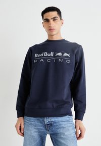 Tamsiai mėlyna ilgomis rankovėmis palaidinė su apvaliu iškirpimu, dekoruota baltu "Red Bull Racing" logotipu. Pagaminta iš minkštos medvilnės mišinio.