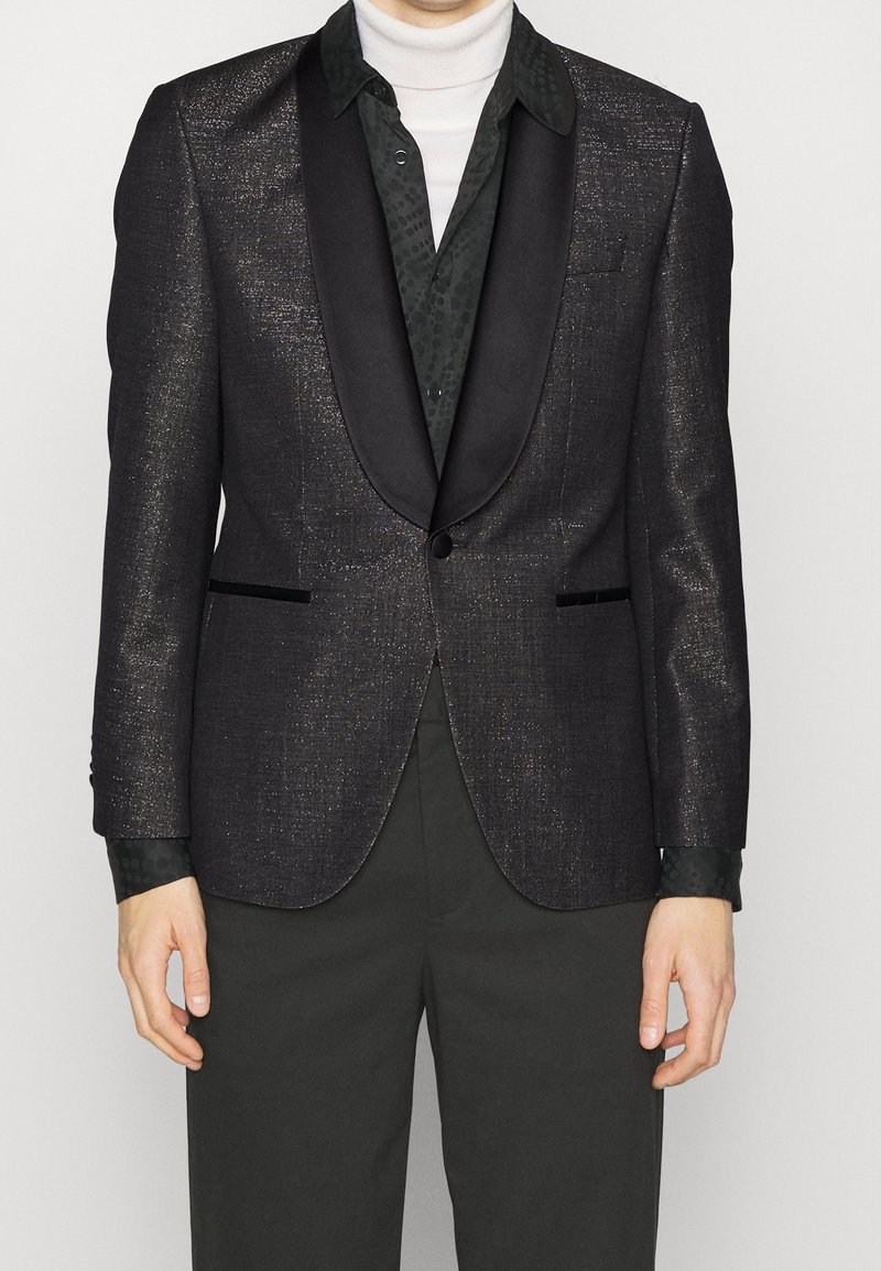 Tuxedo sako ve tmavě šedé látce s jemným leskem, s saténovým šálovým límcem, dvěma předními kapsami a zapínáním na jeden knoflík.