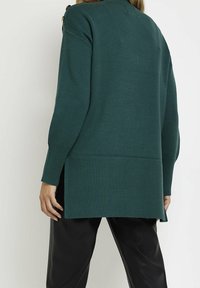 Mörkgrön stickad tröja med ribbad nederkant och ärmslut, med en oversized passform och sidofickor för ökad rörelsefrihet.