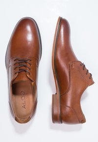 Chaussures de ville en cuir marron avec bouts ronds, design à lacets, finition texturée et talons en bois. Logo positionné à l'intérieur de la chaussure.