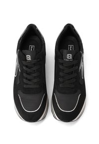 Un paio di sneaker nere con dettagli bianchi, design con lacci e suole bianche spesse, viste dall'alto su uno sfondo bianco.