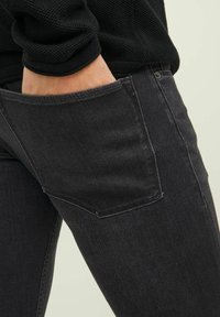 Sorte denimjeans med rett snitt, synlig lomme-søm, og en litt slitt tekstur. Materialet ser holdbart og fleksibelt ut.