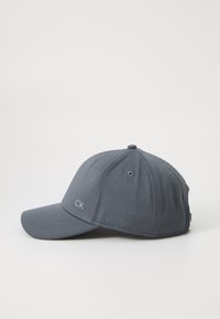 Grijze baseballpet met een gestructureerd ontwerp, mesh-textuur en een gebogen rand. Voorzien van het "CK"-logo in lichtgrijs aan de voorkant.