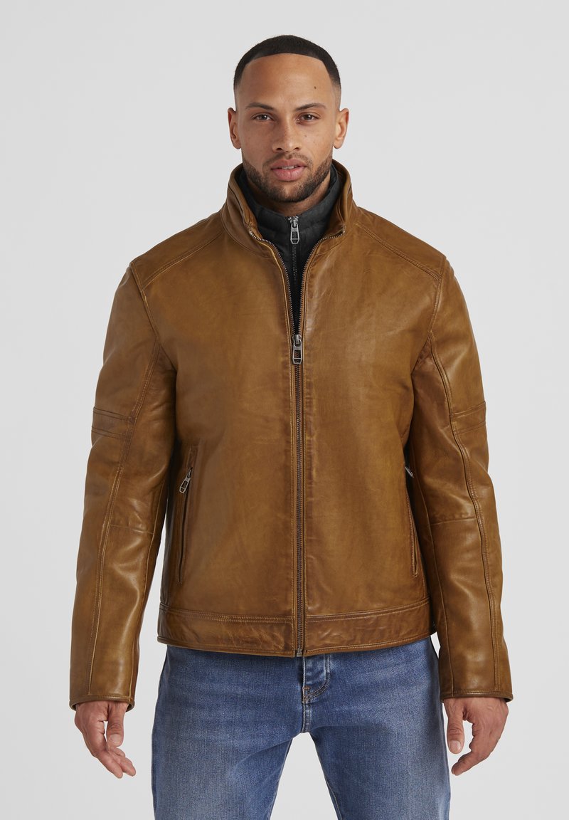 Braune Lederjacke mit hohem Kragen, Reißverschluss vorne, Seitentaschen und glatter Textur, kombiniert mit blauen Jeans.