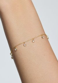 Złota bransoletka łańcuszkowa z pięcioma małymi, okrągłymi, przezroczystymi kryształami zwisającymi z łańcuszka, o delikatnym, cienkim wzornictwie.