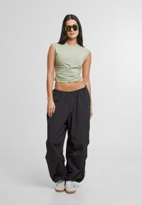 Lichtgroen, kortgevormd crop top met een twistdetail, gecombineerd met losse, zwarte, hoge taillebroeken en witte sneakers.