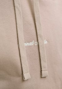 Sudadera beige con cordones y tejido texturizado. La tela suave tiene un acabado liso, con un sutil texto impreso en blanco.