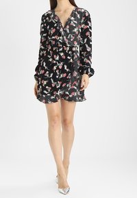 Černé šaty s květinovým vzorem v růžové a bílé barvě, dlouhé rukávy se nařasenými manžetami, výstřih do V a volánový lem. Stříbrné boty doplňují celý outfit.