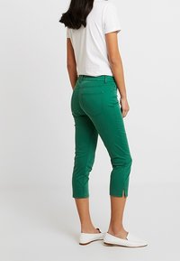 Pantalon court vert à coupe ajustée, en coton, avec des fentes latérales à l'ourlet et des poches arrière. Associé à des chaussures blanches.