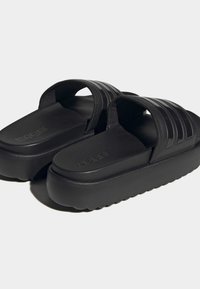 Sorte slidesandaler med en bred rem og struktureret overdel, der har en tyk platformssål og brandlogo på fodsengen.