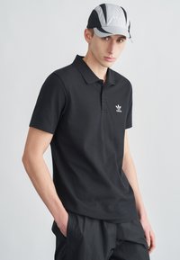 Mustast puuvillast polo-särk lühikeste varrukatega, mille rinnal on valge Adidas logo. Sobitatud halli ja musta mütsiga.