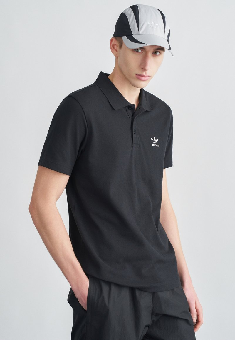 Mustast puuvillast polo-särk lühikeste varrukatega, mille rinnal on valge Adidas logo. Sobitatud halli ja musta mütsiga.