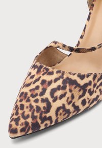 Chaussure plate à bout pointu en tissu imprimé léopard marron et noir avec une fine bride sur l'ouverture du pied sur fond clair.