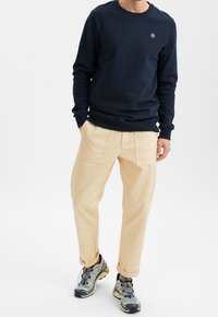 Sudadera azul marino con cuello redondo, puños acanalados, pantalones cargo beige con bolsillos anchos y zapatillas deportivas gris azulado con detalles en negro y amarillo.