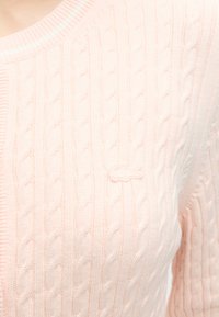 Pull rose clair en maille torsadée avec col rond et logo crocodile brodé discret sur la poitrine.
