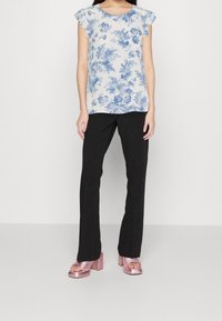 Niebieska bluzka w kwiatowy wzór z falbanami na rękawach, zestawiona z czarnymi spodniami prostymi i różowymi sandałami na słupku.