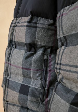 Bunda do půlky s černou horní částí a šedou kostkovanou spodní částí. Má viditelnou černou zipovou kapsu a prošívanou texturu.