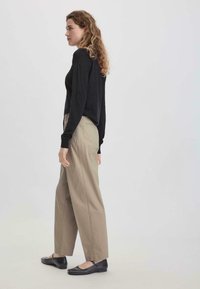 Zwarte long sleeve top gecombineerd met beige wijde pantalon en zwarte flats. De stof is glad en de broek heeft een klassieke snit.