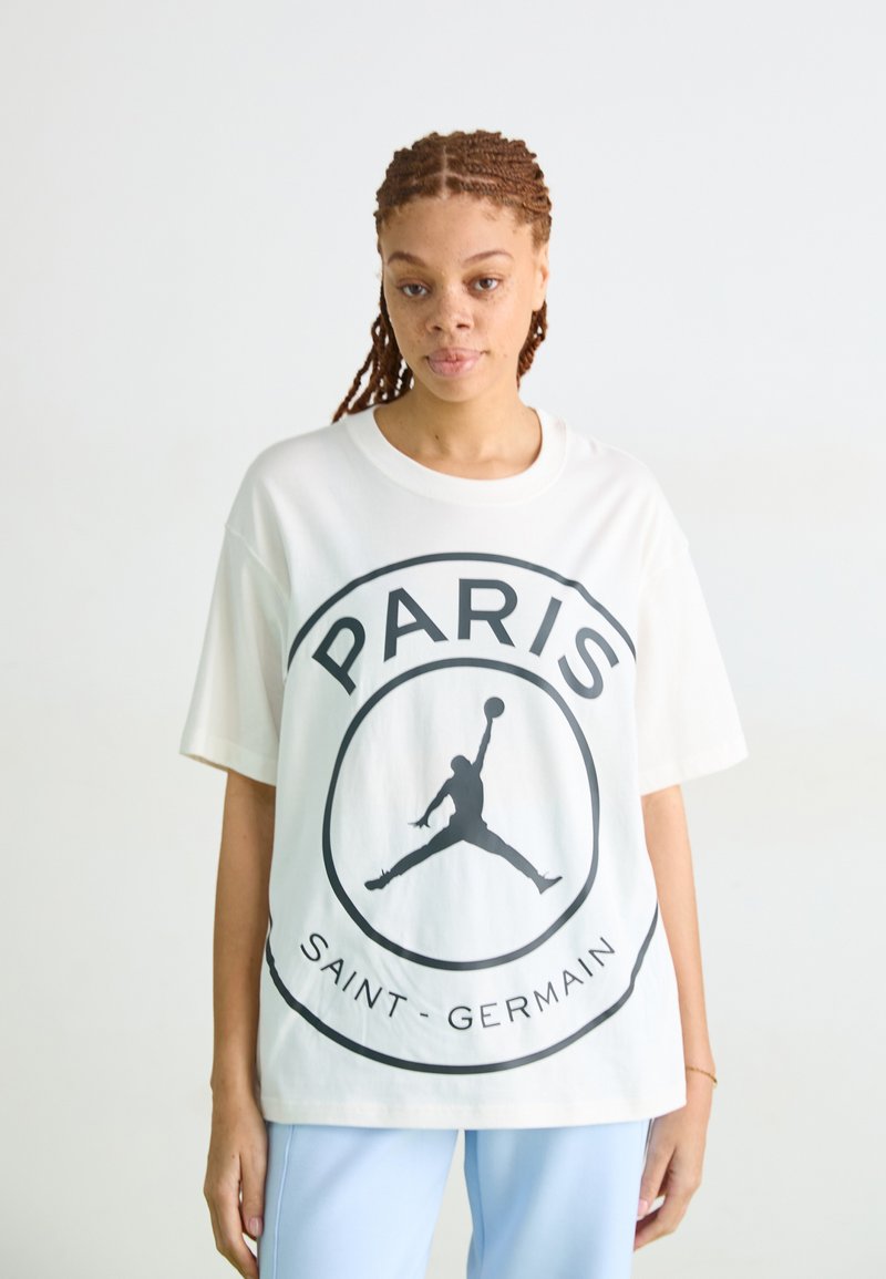 T-shirt oversize blanc avec un imprimé graphique noir du mot "PARIS" et "SAINT-GERMAIN" avec le logo Jordan au centre.