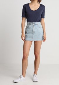 Námořnické tričko s krátkým rukávem v kombinaci se světle modrou džínovou mini sukní s roztrhaným lemem, obuté s bílými teniskami.