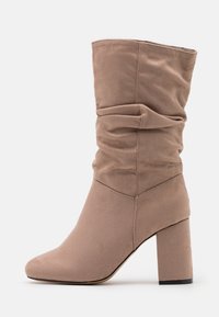 Beige slouch ankle boot made of soft suede with a block heel and pointed toe, featuring gathered texture on the shaft for added detail.