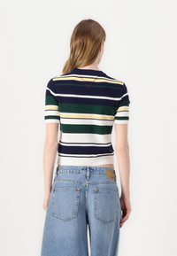 Top in maglia a righe cropped con strisce blu navy, verde e bianco, con scollo a V e dettagli in cucitura rossa sulla schiena. Classici pantaloni shorts di jeans.