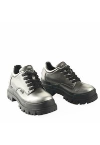 Zapatos de cuero plateado con suelas de goma negra, que presentan un grueso y robusto relieve y cordones negros. Con un logotipo acentuado en la lengua.