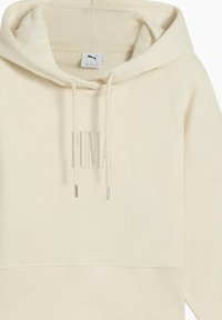 Crème-kleurige hoodie met geribde boord en manchetten. Heeft het PUMA-logo op de voorkant gedrukt en trekkoorden met metalen uiteinden.