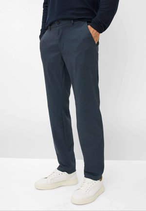 Marineblaue Hose aus strukturiertem Stoff, gerade geschnitten, mit Seitentaschen und Knopfverschluss, kombiniert mit weißen Sneakers.