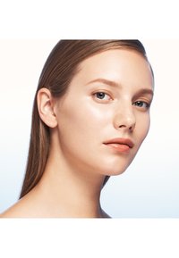 Gros plan sur le visage d'un modèle avec une peau lisse, des cheveux noirs raides, un maquillage léger, des yeux bleus et une couleur naturelle des lèvres, sur un fond dégradé doux.