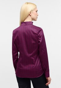 Camicia a maniche lunghe fucsia con un sottile motivo geometrico. Tessuto liscio e lucido, colletto alla coreana e polsini con bottoni. Vestibilità su misura.