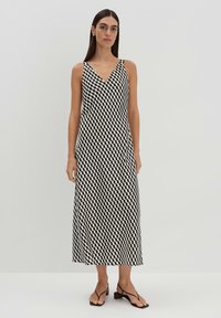 Ärmelloses, V-Ausschnitt-Kleid im schwarz-weißen Hahnentrittmuster. Fließende Silhouette, knielang, weicher Stoff, kombiniert mit minimalen Absatzsandalen.