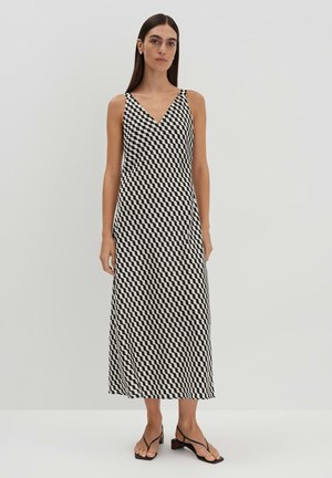 Robe sans manches, décolleté en V dans un motif pied-de-poule noir et blanc. Silhouette fluide, longueur mi-mollet, tissu doux, associée à des sandales à talons minimalistes.