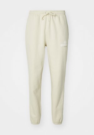 Világos bézs szabadidőnadrág puha anyagból, elasztikus derékkal, zsinórral, cuffolt bokákkal és apró nyomtatott logó részlettel.