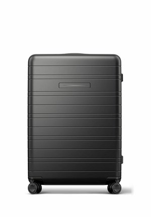 Black hard-shell suitcase with horizontal ridges, four swivel wheels, and a recessed handle on the top side.
