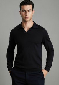 Pulover lung cu mânecă lungă, de culoare neagră, cu guler în formă de V și guler plat. Textură moale, design ajustat și manșete și margine ribbate. Fără modele sau accente vizibile.