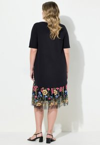Camiseta negra de manga corta combinada con una falda sheer bordada en flores y colores que presenta tela negra y varios patrones de flores.