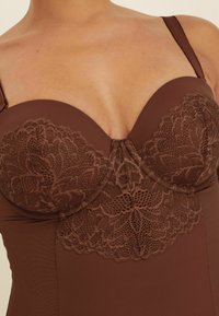 Bruine kant bodysuit met een gestructureerde top, voorzien van bloemenkantdetails, gladde stof, verstelbare bandjes en een diepe halslijn.