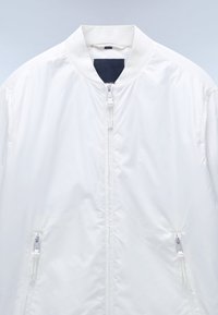 Witte bomberjack met een ritssluiting aan de voorkant, ribgebreide kraag en twee ritszakken aan de zijkant. Glad, lichtgewicht stof met een minimalistisch ontwerp.
