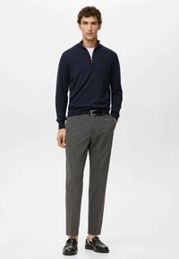 Granatowy sweter z zamkiem przy szyi, szare spodnie o fakturze, czarny pasek i błyszczące czarne mokasyny; minimalistyczny design, dopasowany krój, gładka faktura.