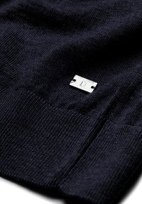 Navy gestrickter Pullover mit einem silbernen rechteckigen Etikett mit einer eingravierten "D", das eine glatte Textur und ein vielseitiges Design hervorhebt.