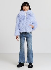 Giacca in pelliccia sintetica di colore viola chiaro con colletto alto e chiusura a zip. Abbinata a jeans blu a zampa d'elefante e scarpe con piattaforma nere.